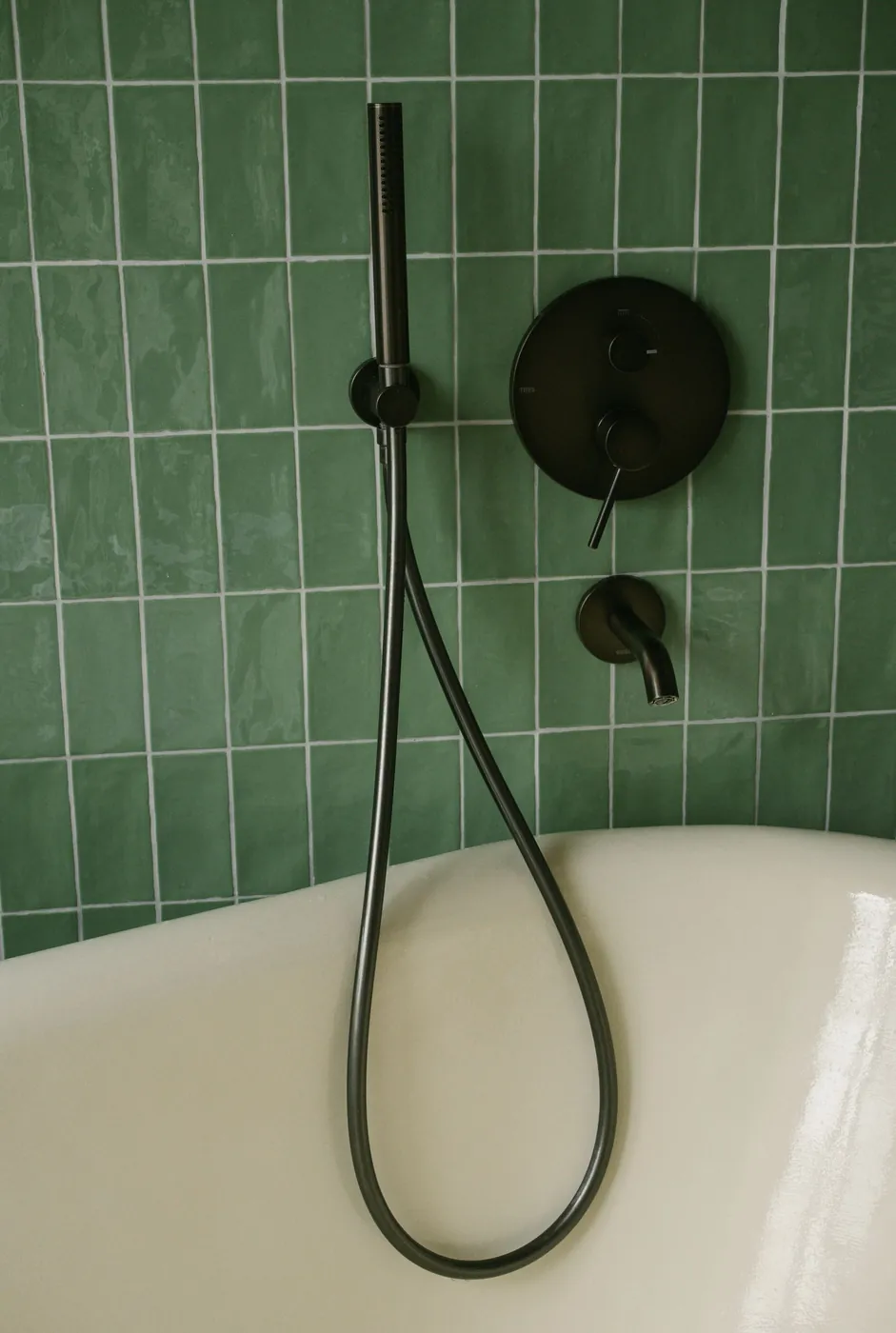 Wit bad tegen groene tegels met zwarte kranen