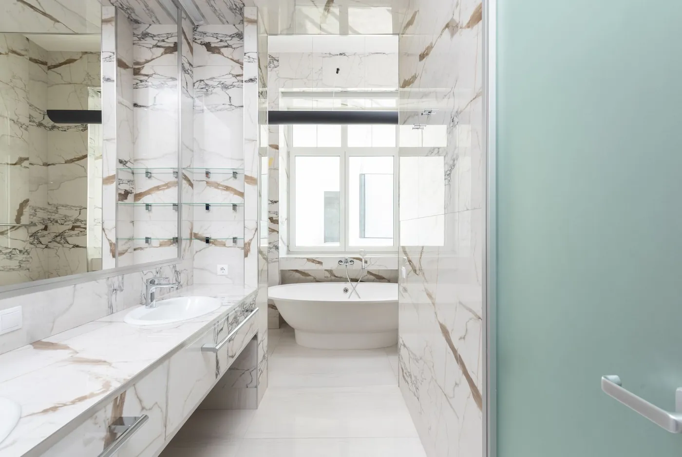 Lichte badkamer met marmeren wanden, wastafel en bad bij het raam