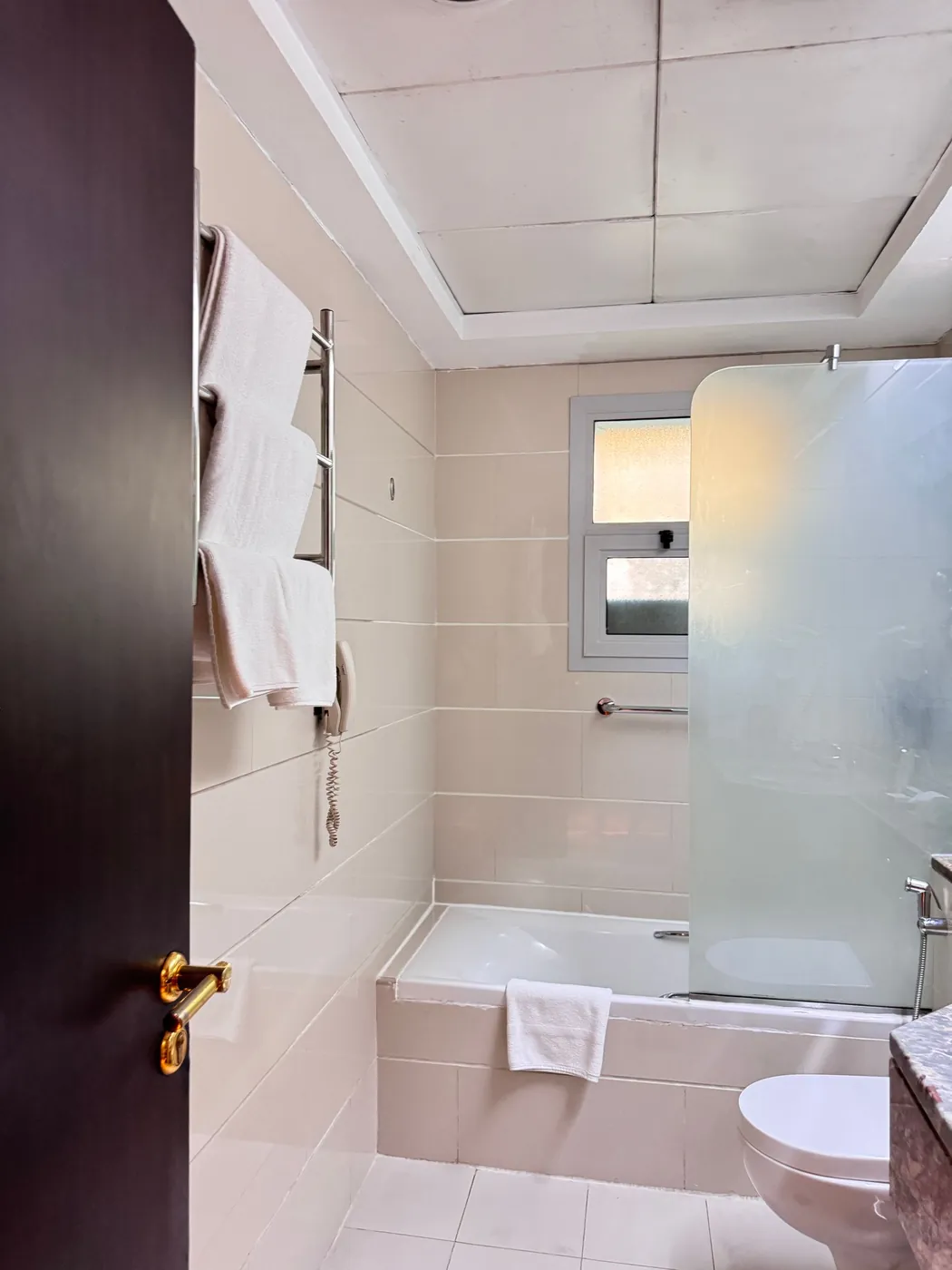 Compacte badkamer met beige tegels, glazen douchewand en handdoeken